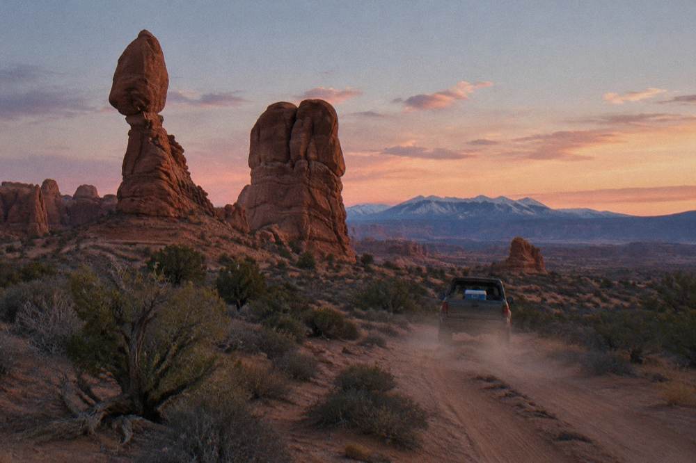 Wide desert view of layered red rock formations stretching to a distant horizon at dusk.