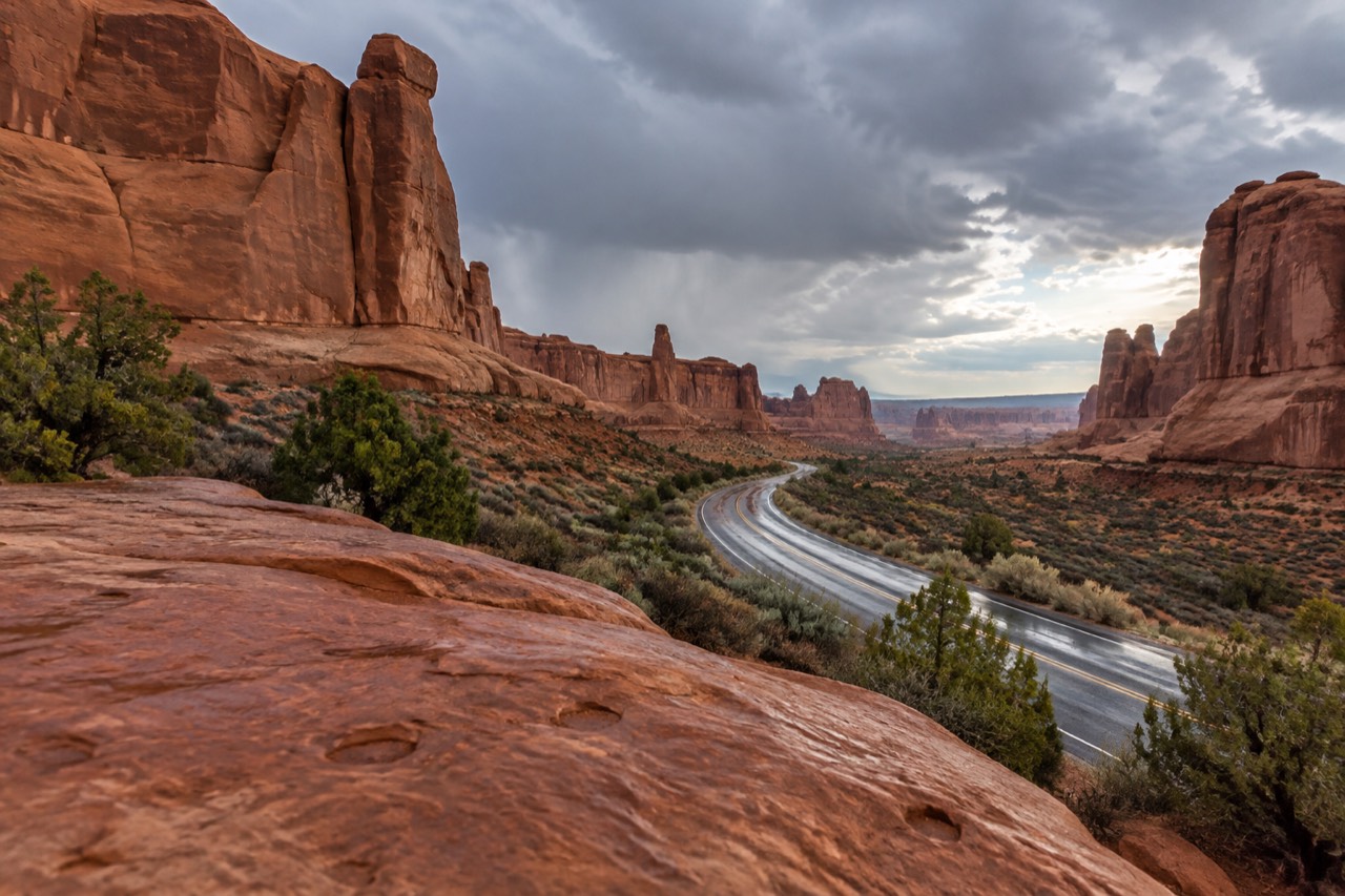 Red rock fins and sandstone arches rising above a winding paved road in high desert country.