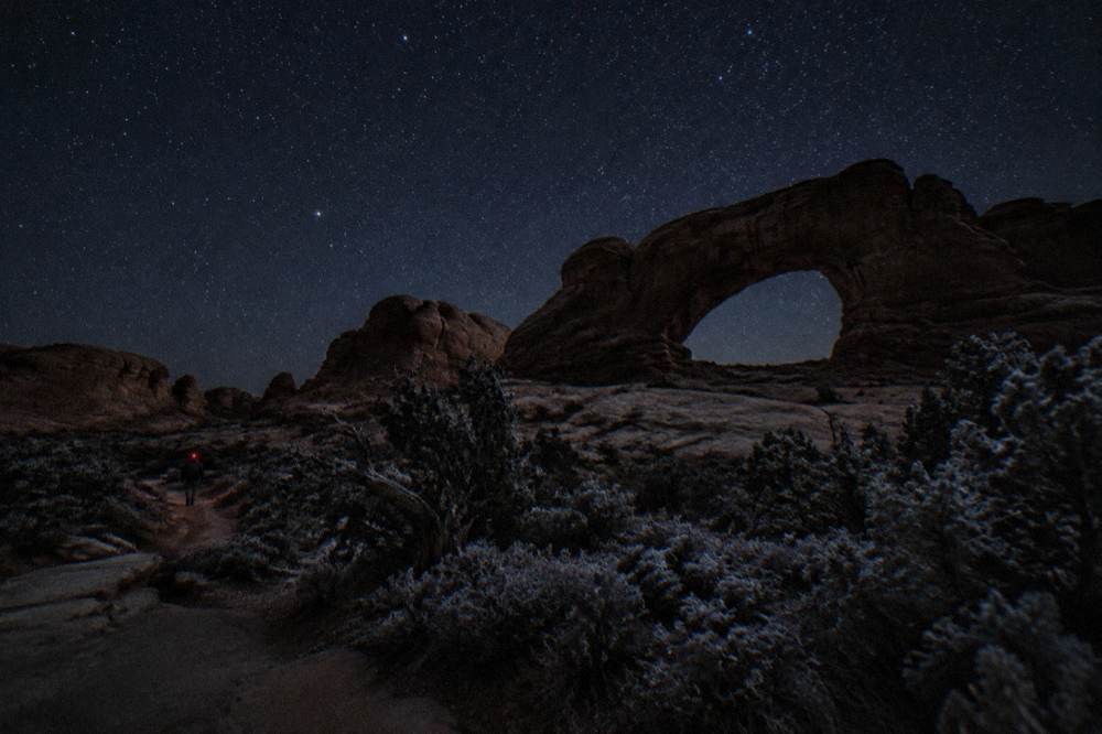 Stars filling a dark night sky above the silhouette of a sandstone arch formation