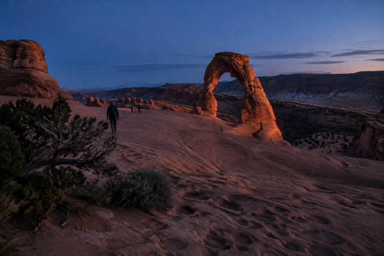 Delicate Arch glowing warm orange against a deep blue evening sky over smooth sandstone rock