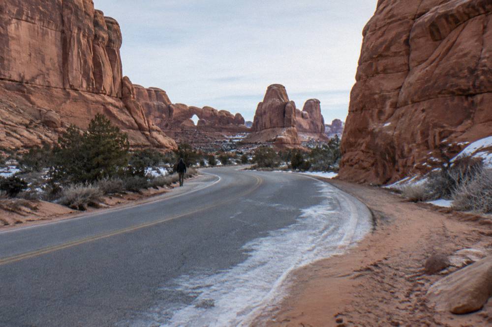 A paved park road curving between tall red sandstone walls near Moab