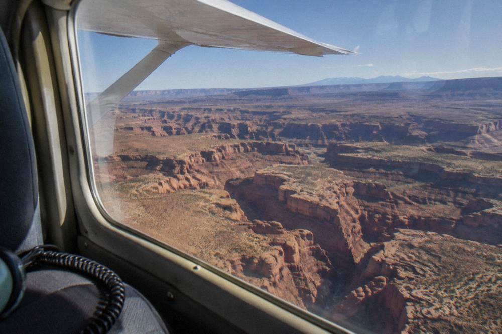 A small airplane wing above a maze of red rock canyons and distant mesas