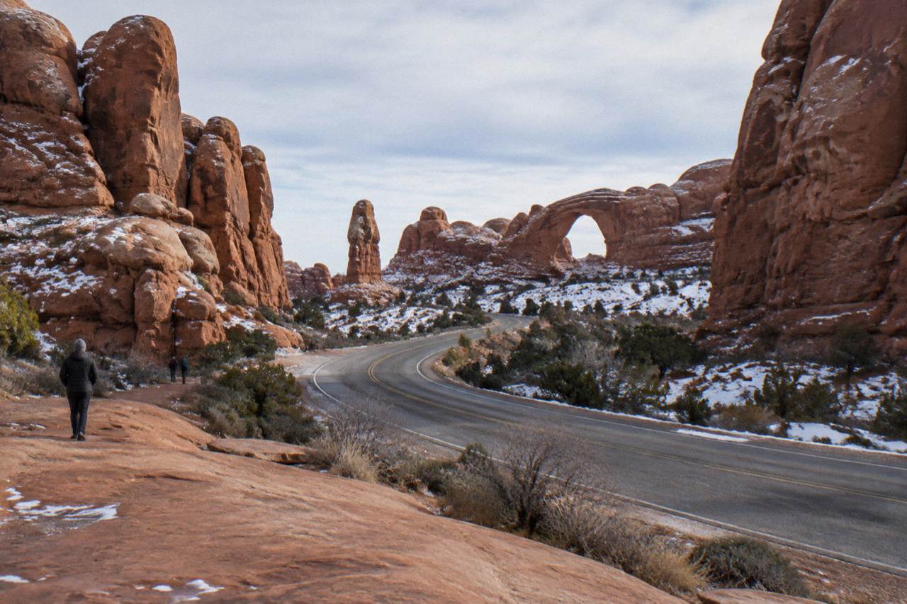 Red rock fins and sandstone arches rising above a winding desert road at golden hour