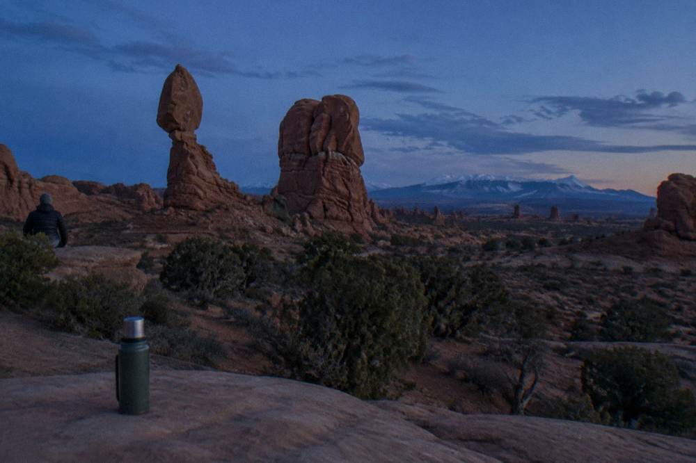 A wide desert overlook with layered rock fins and distant mountains under a deep blue evening sky