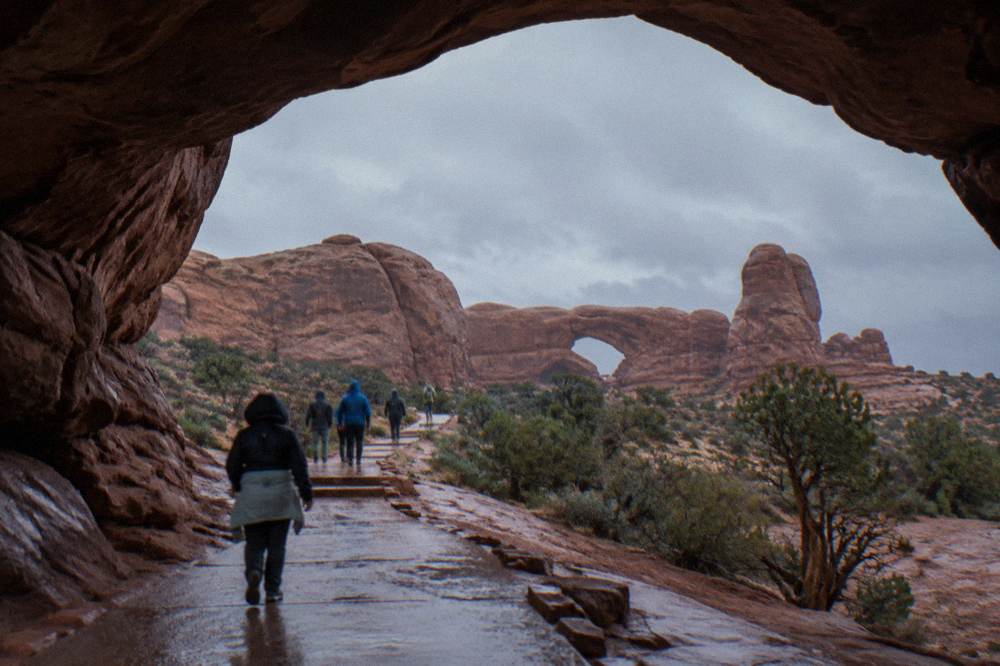 Visitors walking a paved path toward sandstone arches in morning shade