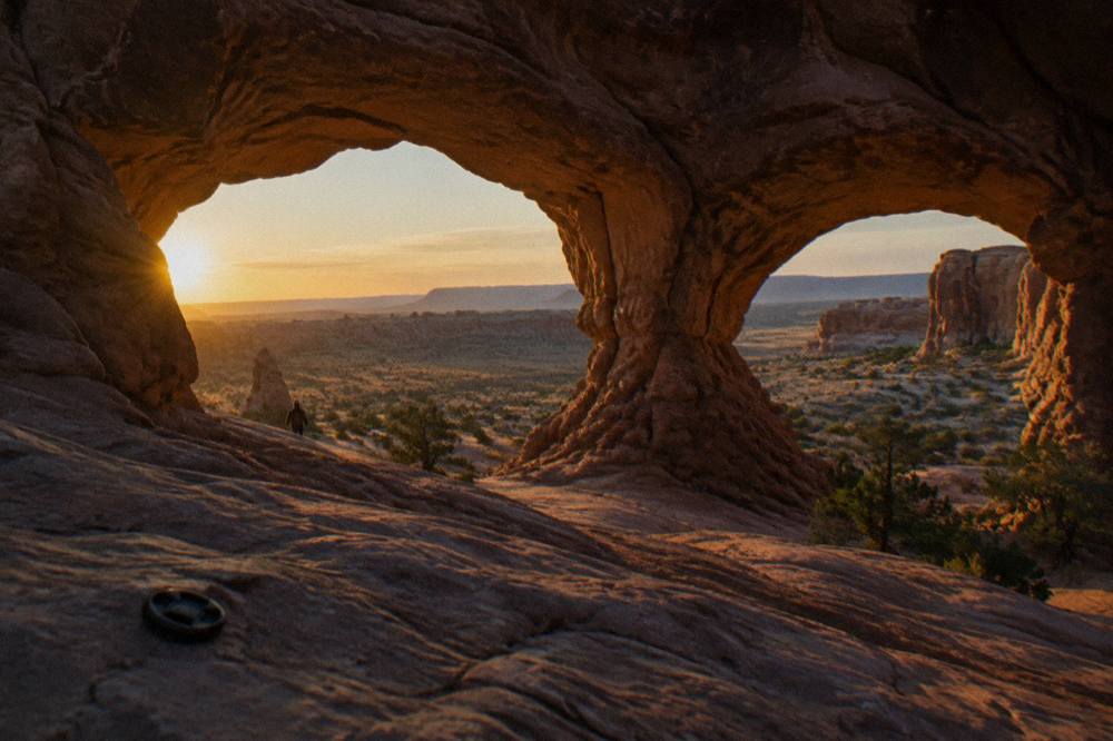 A wide sandstone arch framing an empty desert valley at golden hour