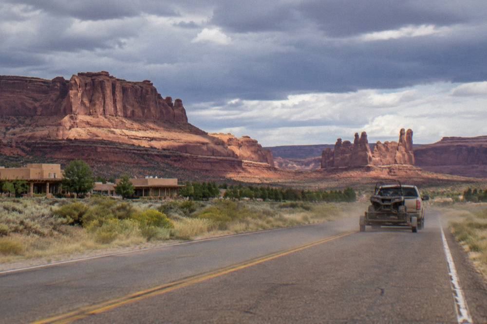 A desert highway stretching toward tall red rock cliffs under afternoon clouds