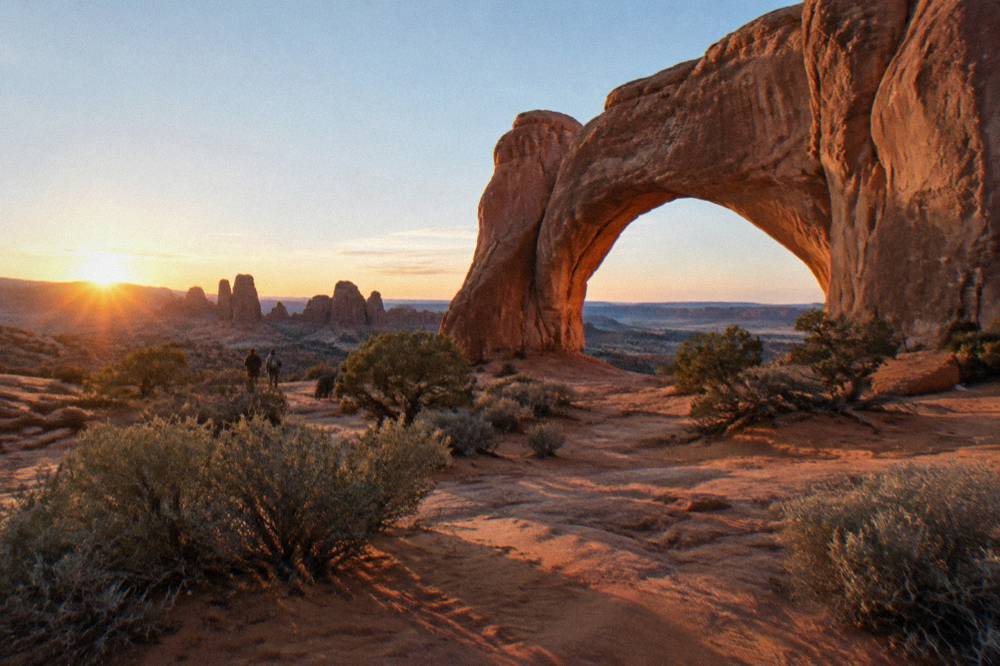 A sandstone arch framed by canyon country terrain under a clear sky