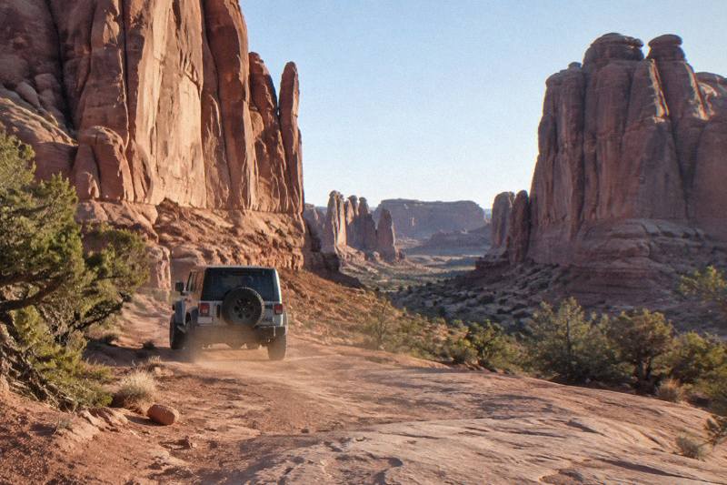 Four wheel drive vehicle on a rocky slickrock trail beneath tall sandstone fins in Arches National Park, Utah
