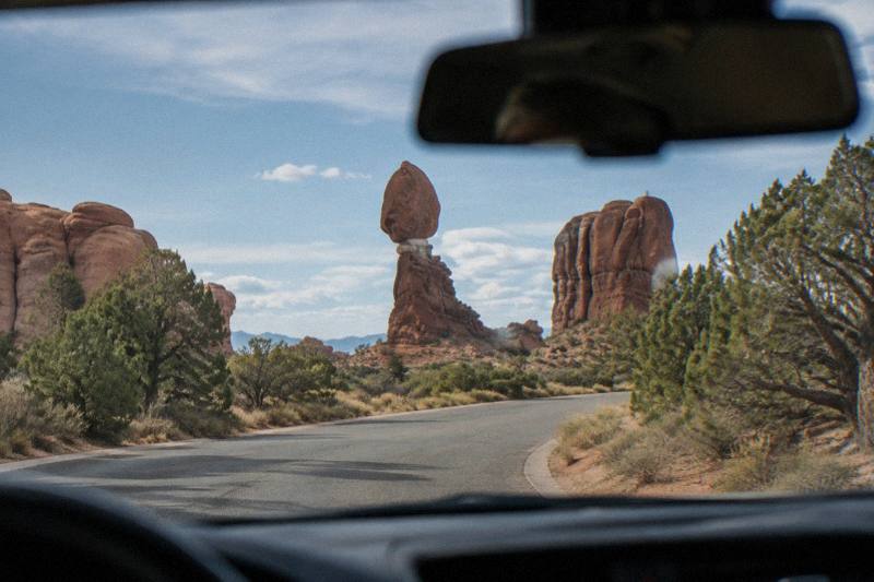 Smartphone mounted on a car dashboard showing an audio tour map at Arches National Park, Utah