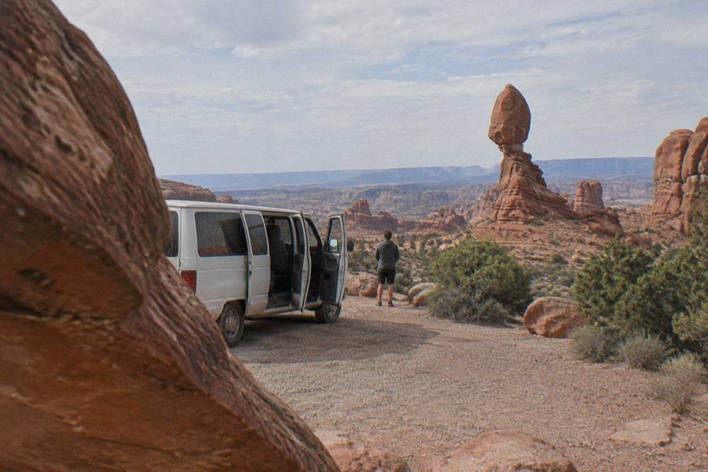 A passenger van parked at a red rock overlook with canyon mesas in the distance