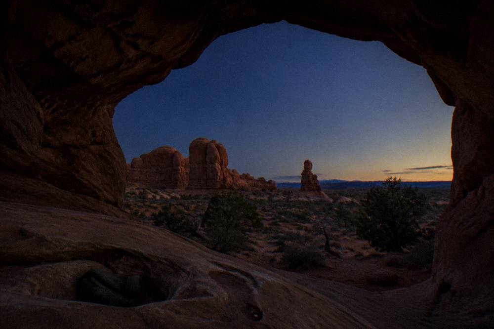 A stone arch framed by dark rock walls under a deep blue evening sky