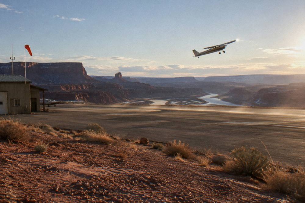 A small airplane banking over wide red rock canyons and river bends at golden hour