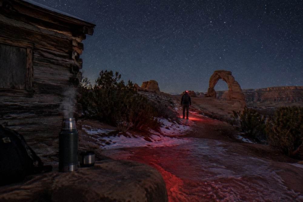 Red headlamp glow on a rock trail edge under a starry sky