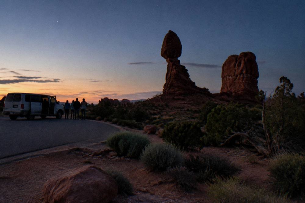 Small group of visitors standing beside a tour van at a dark overlook