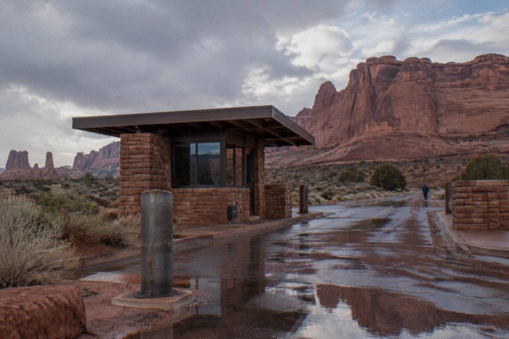 Entrance station booth at Arches National Park with red rock cliffs behind it