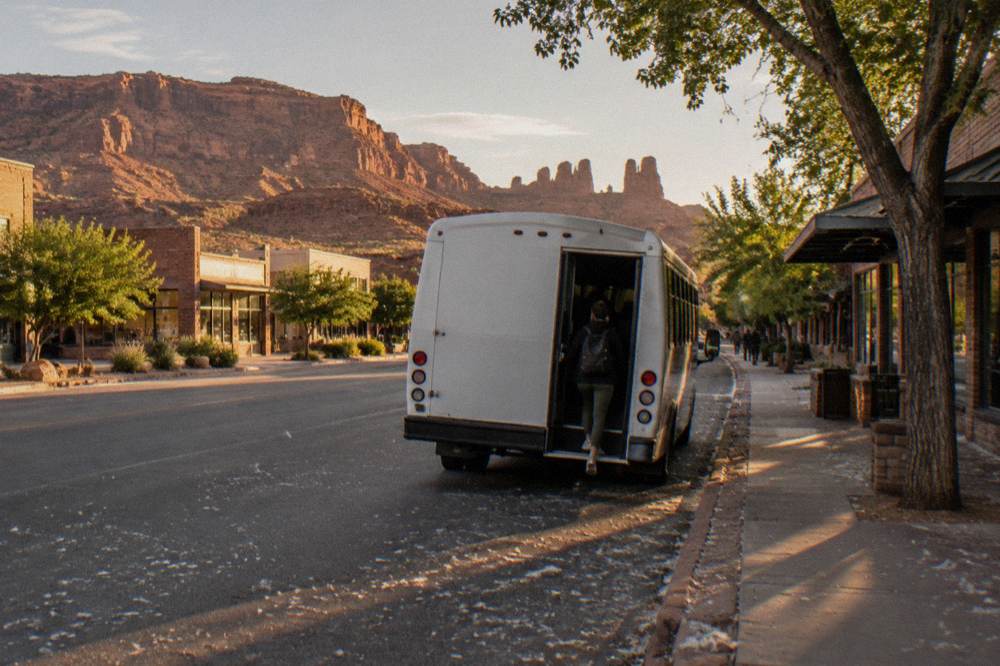 Shuttle bus at a stop with red rock formations in the distance near Moab