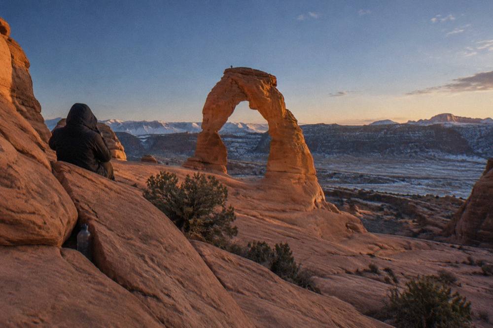 Telephoto view of a lone sandstone arch glowing orange against a deep blue evening sky