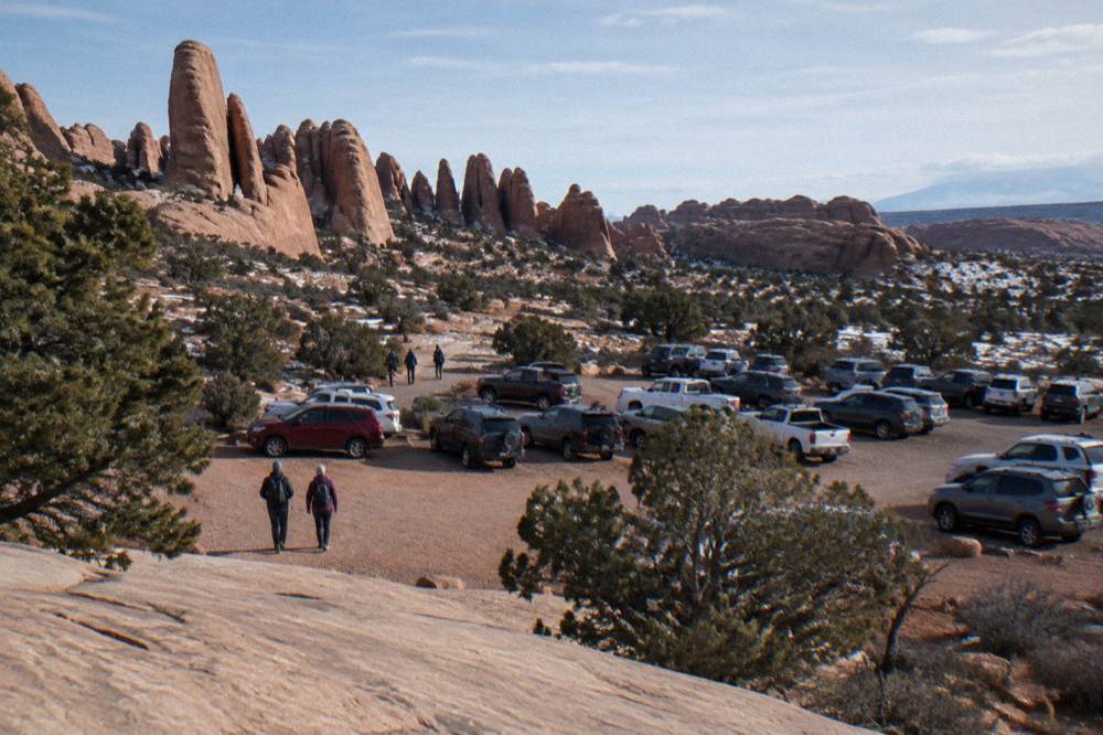 Parking lot near sandstone fins with visitors walking toward a trailhead
