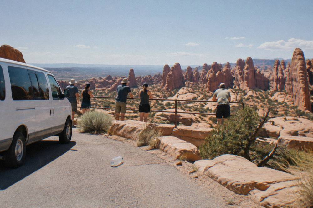 Guided tour van parked at an overlook with passengers standing at a railing