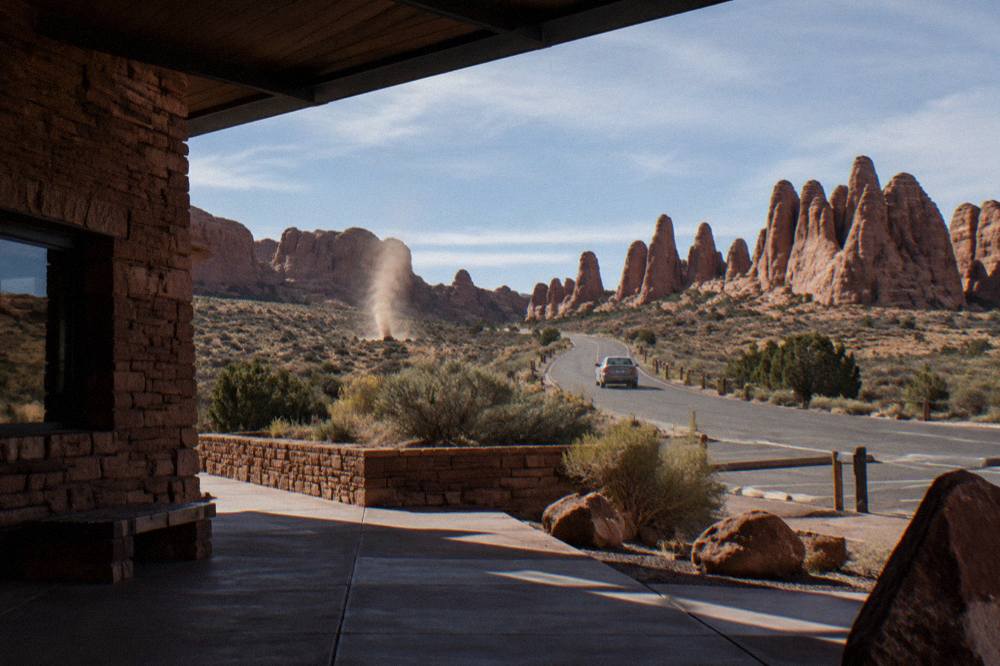 The entrance road to Arches National Park curving toward red sandstone formations under a wide sky