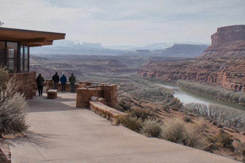Layered sandstone cliffs dropping into a wide river canyon at midday