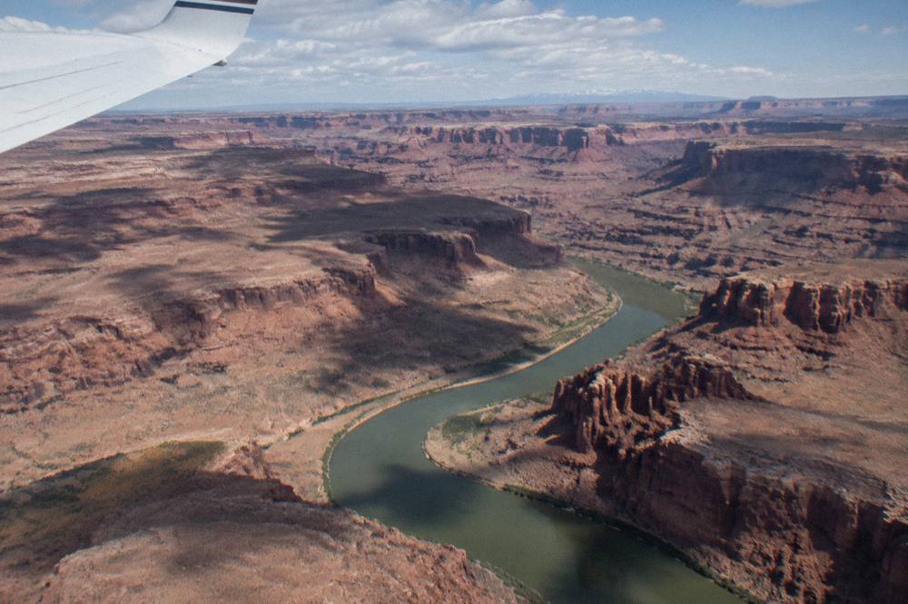 Small airplane wing above red rock canyons and a winding river far below