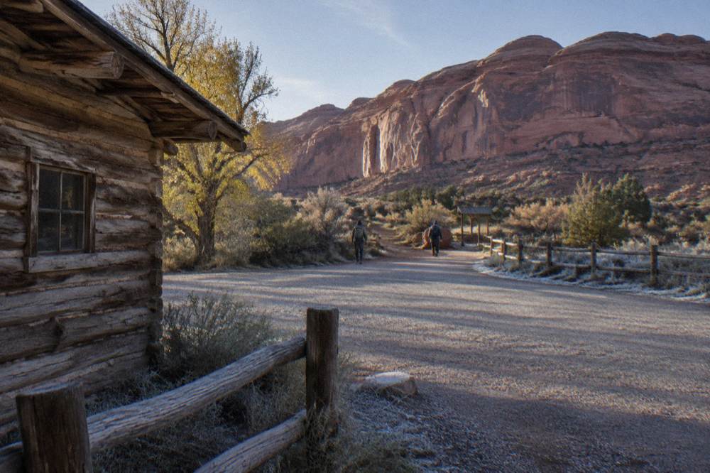Gravel parking area near a trailhead sign with red rock cliffs behind it