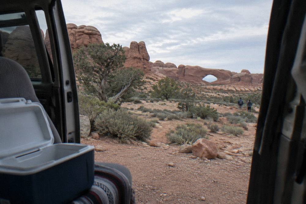 A van parked at a scenic pullout with wide views of red rock arches