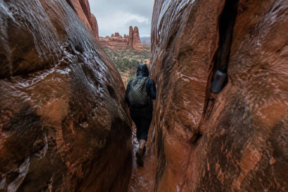 Hiker squeezing through a narrow slot between smooth sandstone walls
