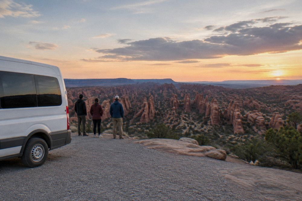 A guided van parked at a red rock overlook with tour guests' water bottles on a bench
