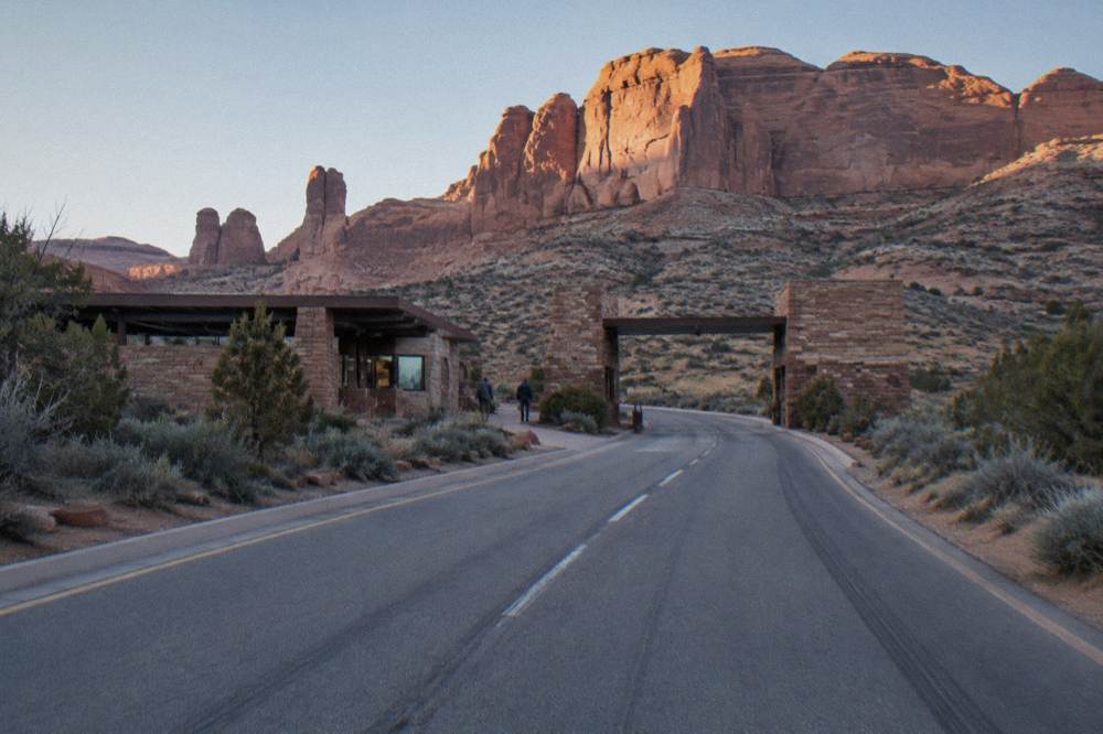 The entrance station road heading toward tall sandstone cliffs at the Arches park boundary