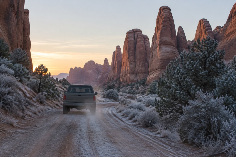 A four-wheel-drive tour vehicle traveling a dirt track between tall red rock fins