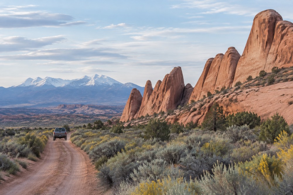 Small unmarked 4x4 pickup on the sandy Willow Springs road past sagebrush, Klondike Bluffs fins and snow-dusted La Sal Mountains