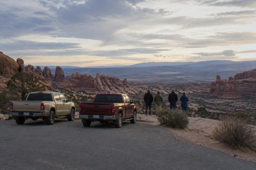 Tour vehicles parked at a sandstone overlook while guests look out over a red rock valley