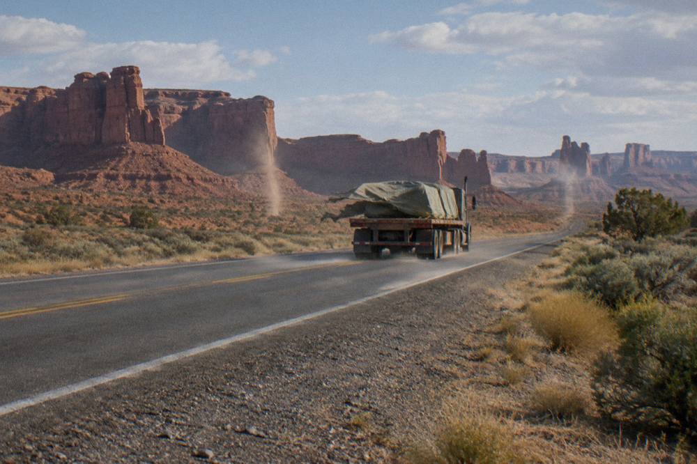 A two-lane desert highway stretching toward orange sandstone formations under a wide sky
