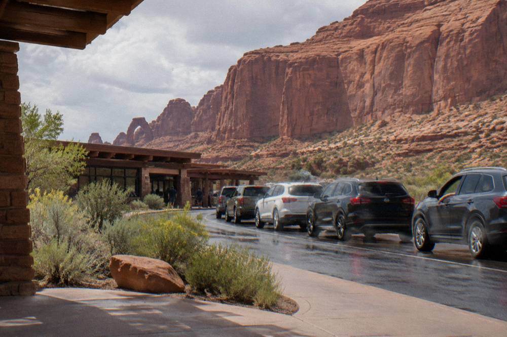 A line of cars waiting at a small entrance station booth beneath red rock walls