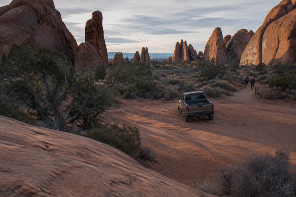 A small dirt parking area beside tall sandstone fins under morning light