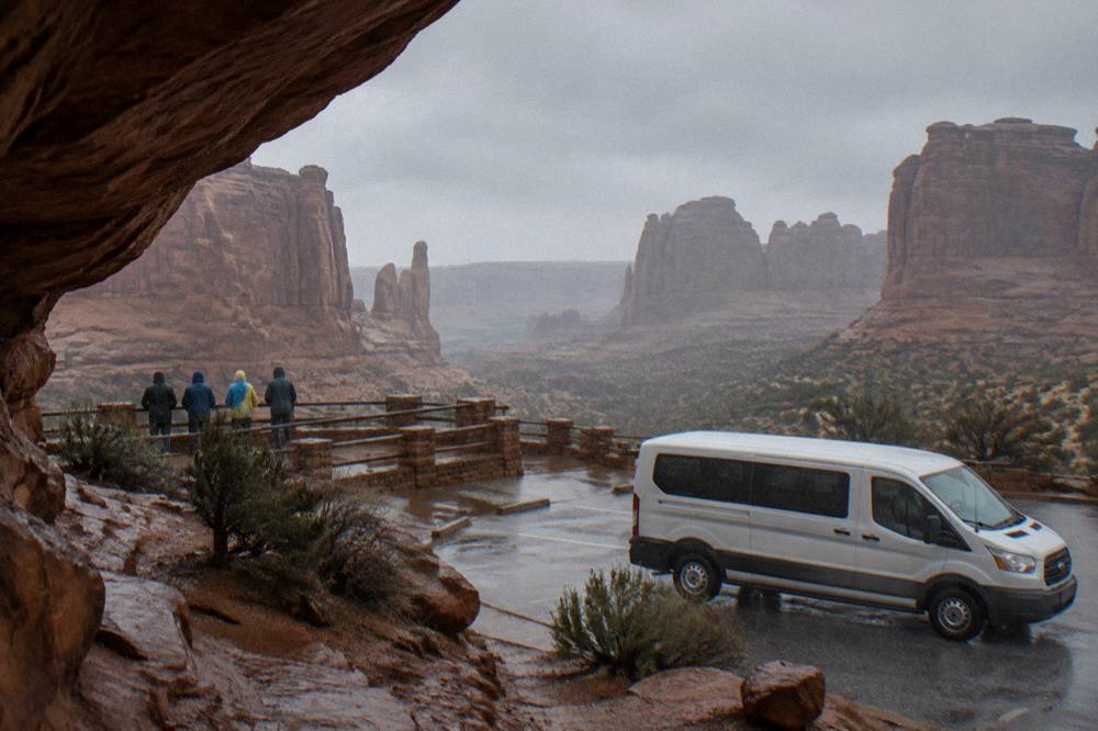 A guided tour van parked at a scenic overlook while guests stand at a railing