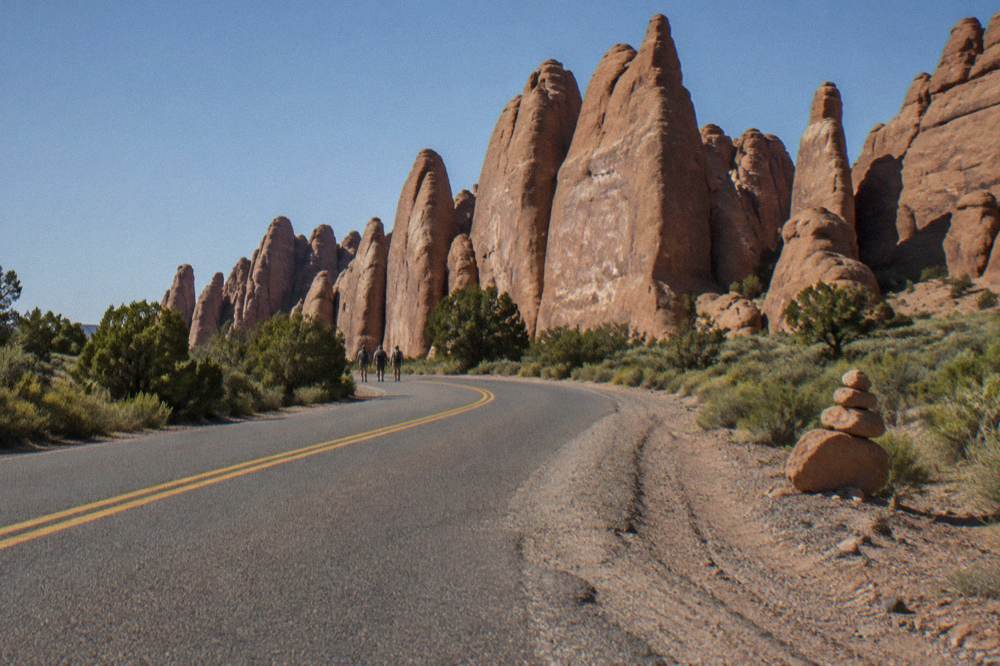 A desert highway curving toward tall sandstone fins under a clear sky
