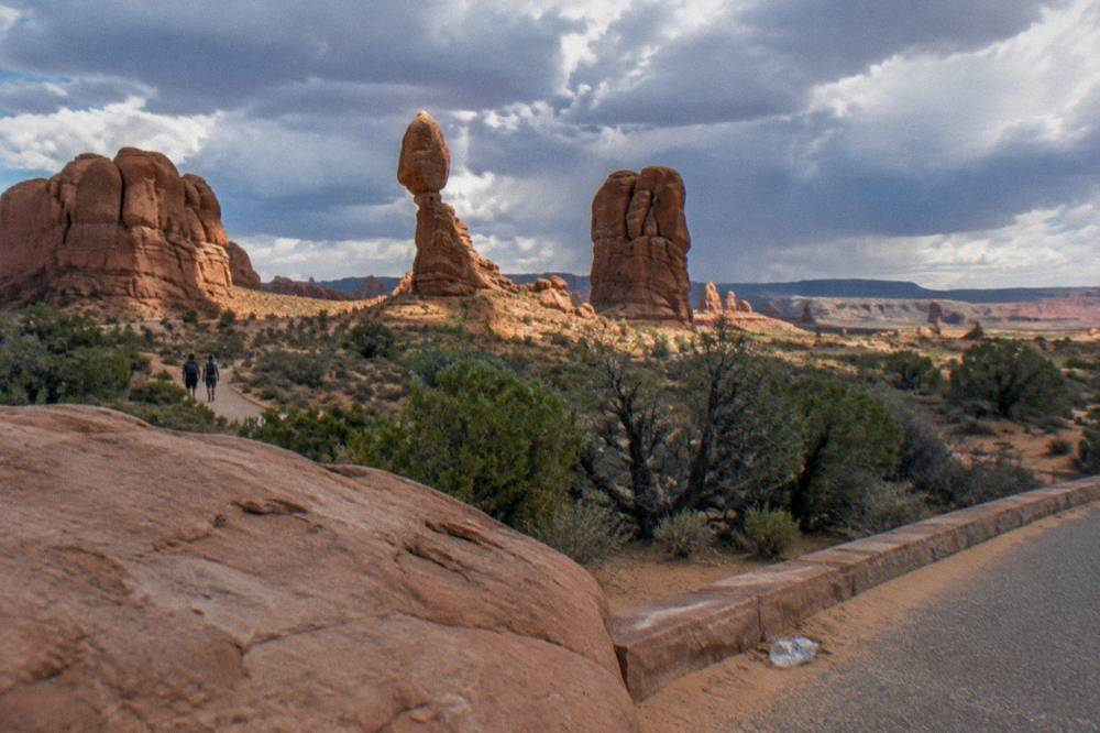 A wide desert landscape of red rock spires and distant mesas at midday