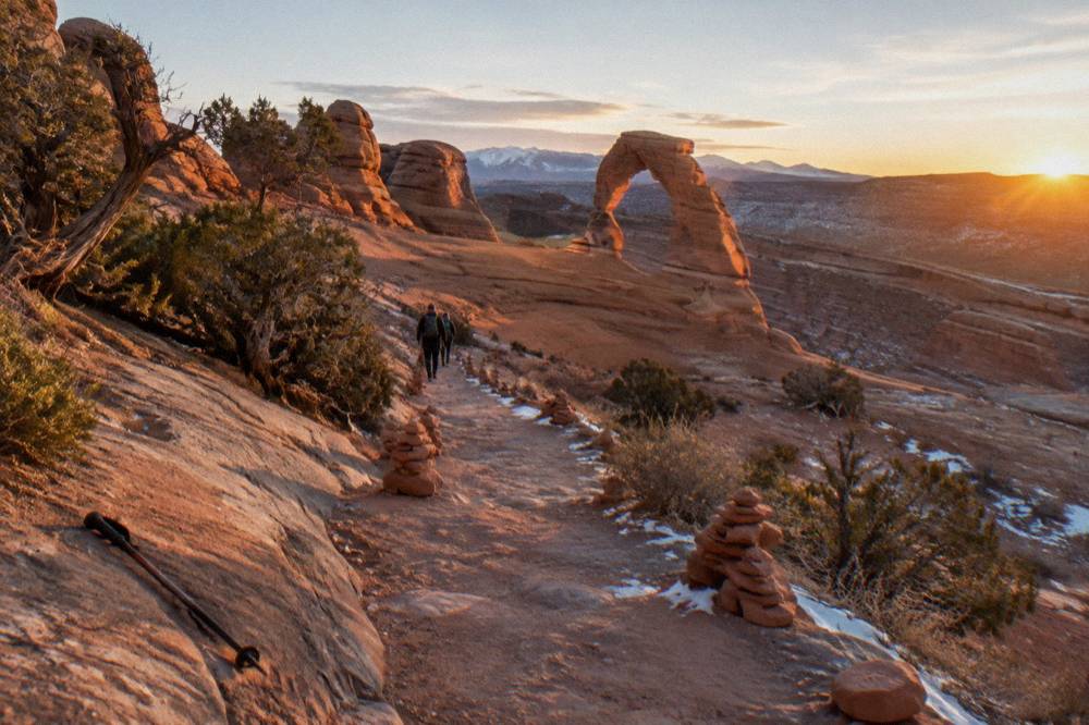 An empty sandstone trail winding toward a large desert arch at golden hour