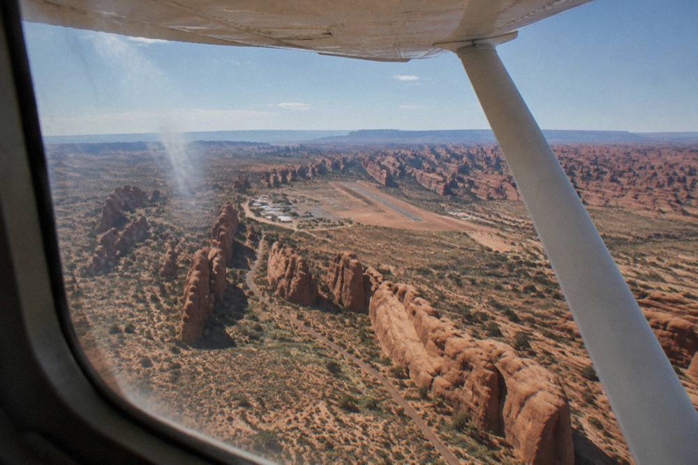A high-wing sightseeing airplane window view of red sandstone fins and canyon country stretching to the horizon.
