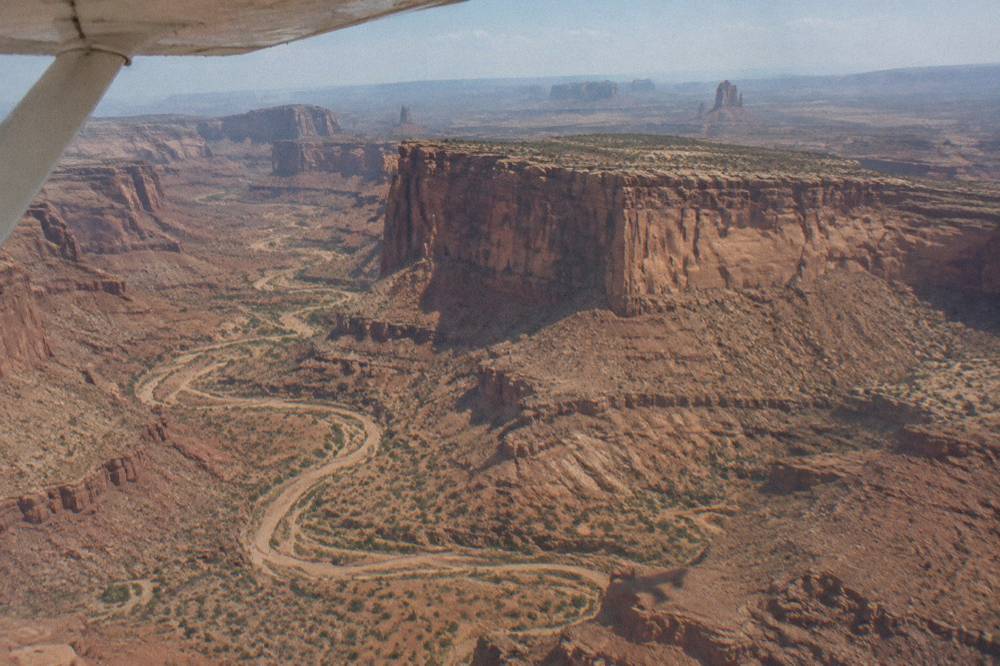 A red rock mesa and winding canyon seen from a small airplane at midday.