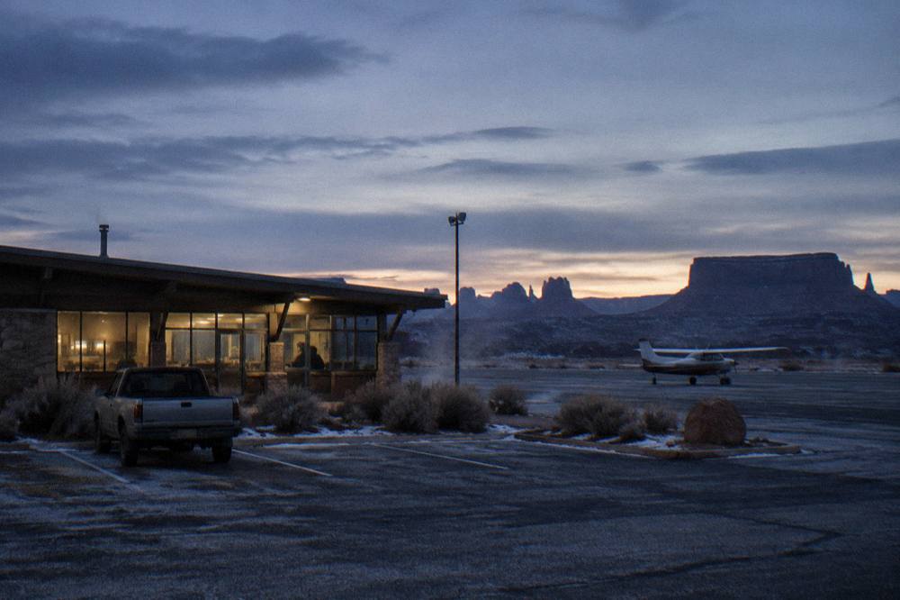 A small airport terminal building at dusk with red rock mesas on the horizon.