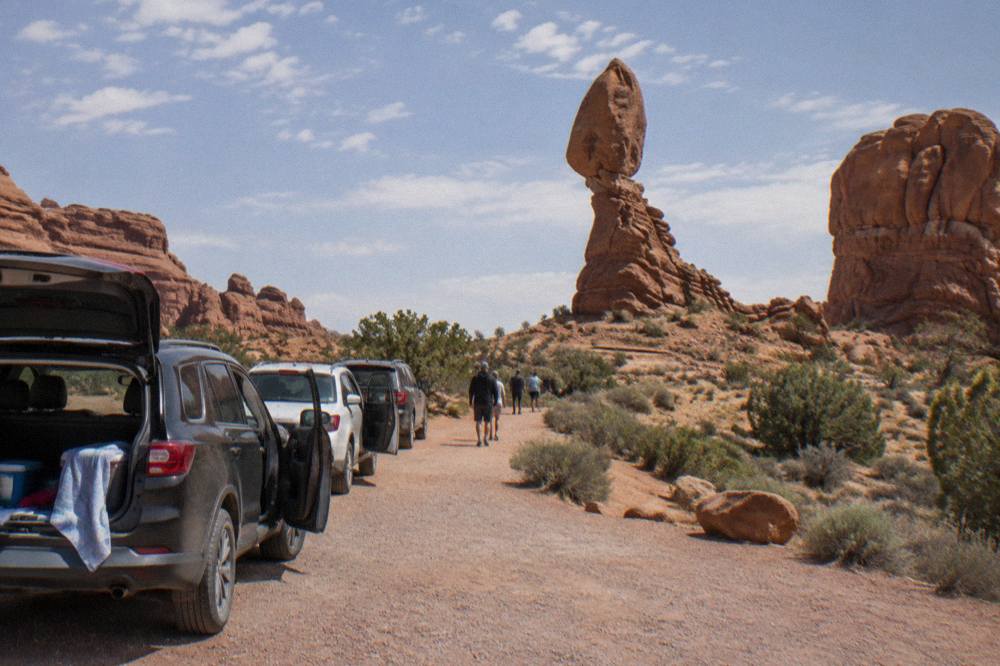 A line of cars parked at a red rock overlook beside a curving desert highway