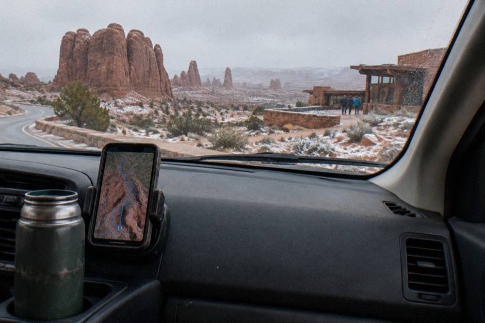 A smartphone mounted on a car dashboard showing a route map through red rock country