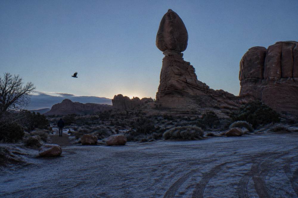 An empty gravel pullout beside tall red rock towers in early morning shade at Arches National Park