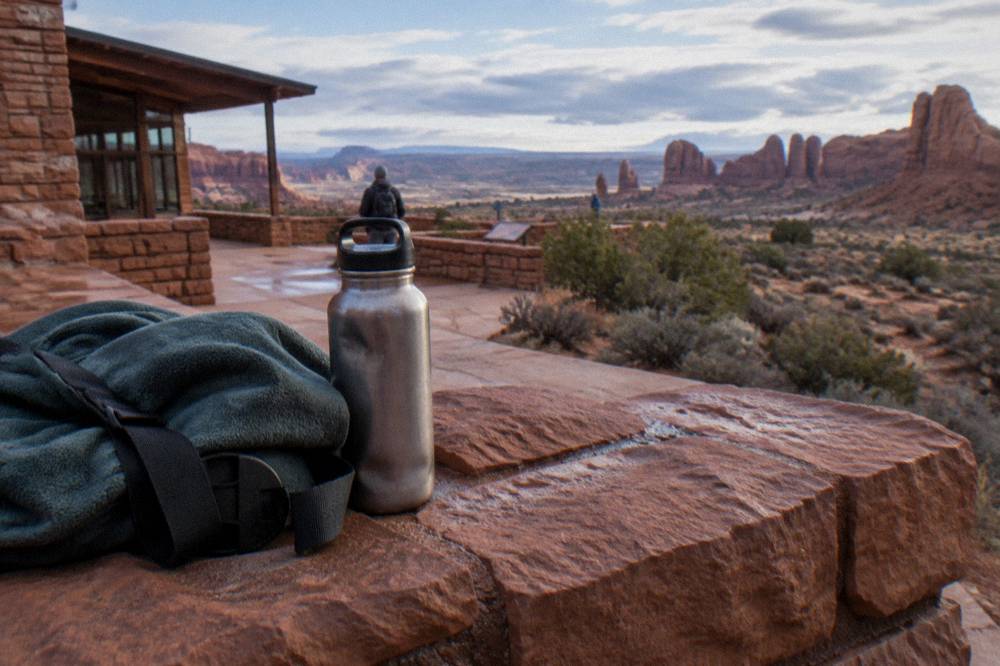 A jacket and water bottle resting on red sandstone rock in cool morning shade at Arches National Park