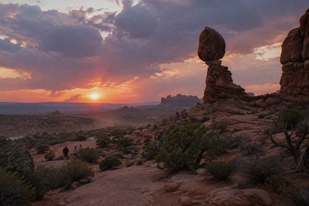 A wide desert horizon with the sun low and storm clouds catching pink light